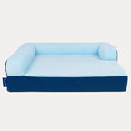 A blue and light blue dog bed with a high bolstered backrest and sides, shown from a front angle on a light gray background. A small blue tag on the left side displays the brand 'PUPPO'.