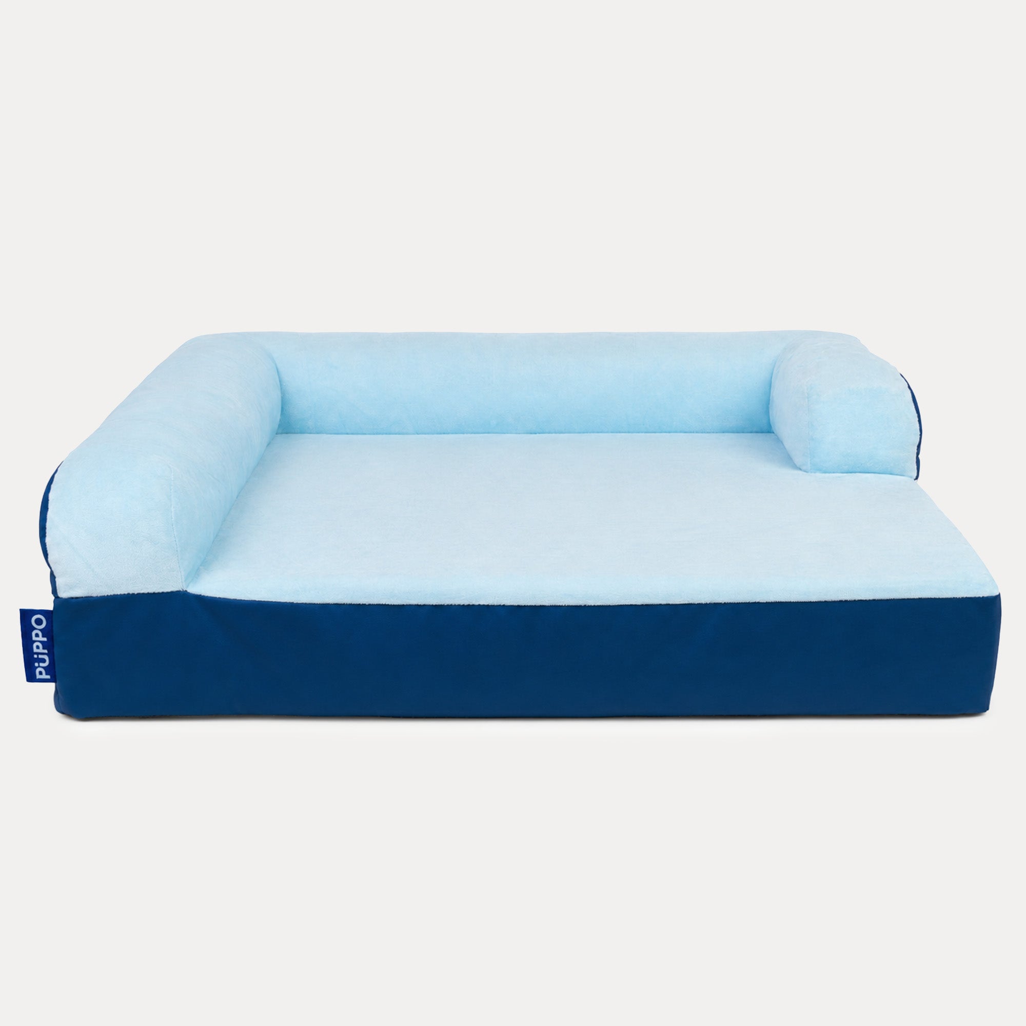 A blue and light blue dog bed with a high bolstered backrest and sides, shown from a front angle on a light gray background. A small blue tag on the left side displays the brand 'PUPPO'.